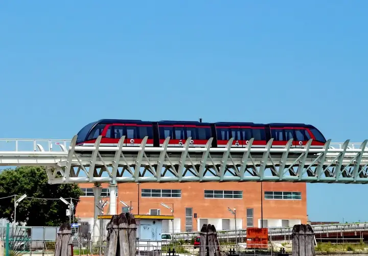 Le people mover de Venise, un train rouge et noir, circule sur une voie aérienne devant un bâtiment orange.