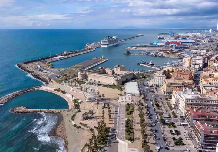 Vue aérienne du port de Civitavecchia, avec un immense paquebot de croisière, des bateaux, une forteresse historique et une grande roue.