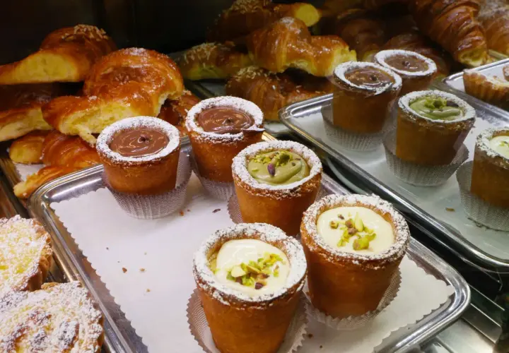 Pâtisseries variées, dont des croissants dorés et des petits gâteaux garnis de crème au chocolat, de pistache ou de crème pâtissière, dans un restaurant florentin.
