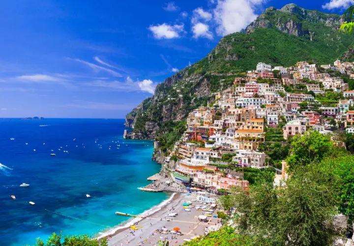 Vue spectaculaire de Positano, une ville pittoresque perchée sur une falaise en **Agerola, Italie**. Les maisons colorées descendent vers une plage animée et la mer d'un bleu profond.