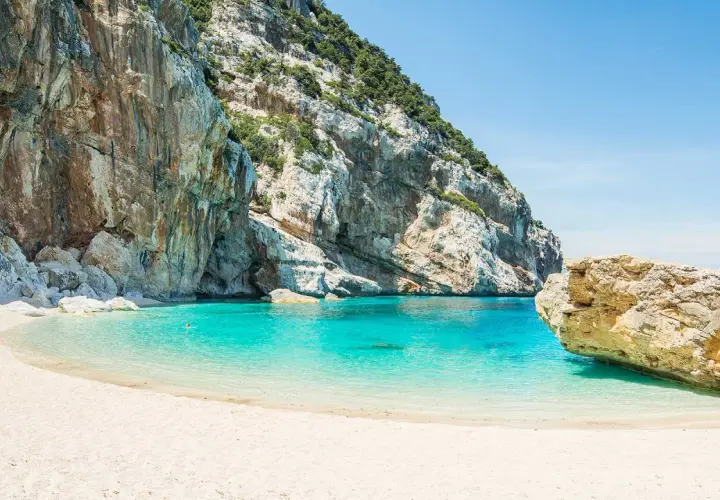 Plage de sable blanc bordée par des falaises imposantes et une eau turquoise cristalline. Un aperçu de ce à quoi ressemble la Riviera italienne.