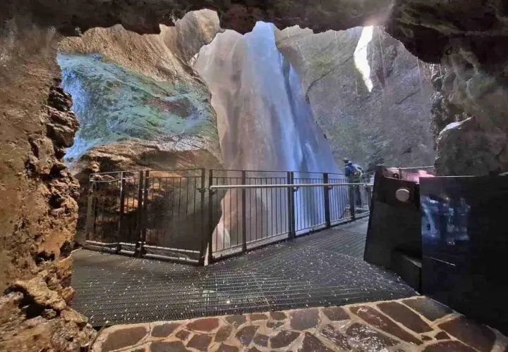Vue depuis une grotte sur la cascade du Varone, avec une passerelle et un visiteur admirant la chute d'eau.