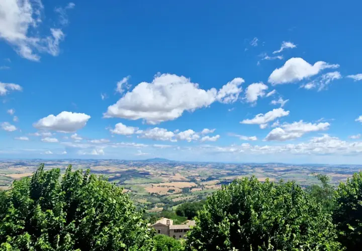 Vue panoramique depuis Cingoli, avec des champs ondulants et un ciel bleu parsemé de nuages blancs.