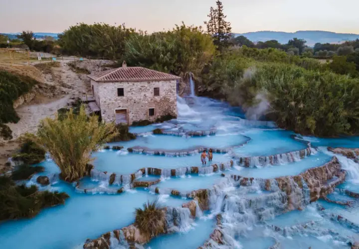 Casciana Terme : un couple se promène dans les cascades d'eau thermale bleue, près d'une vieille bâtisse en pierre.