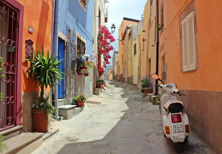 Ruelle colorée en Italie, parfaite pour une location de villa. Un scooter blanc attend, prêt pour l'aventure.