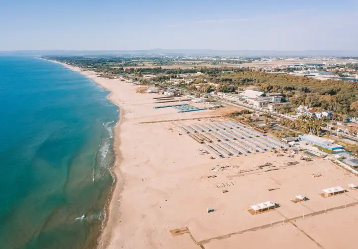 Vue aérienne d'une longue plage de sable fin bordée par la mer bleue, avec des rangées de parasols et des bâtiments à Catane, Sicile.
