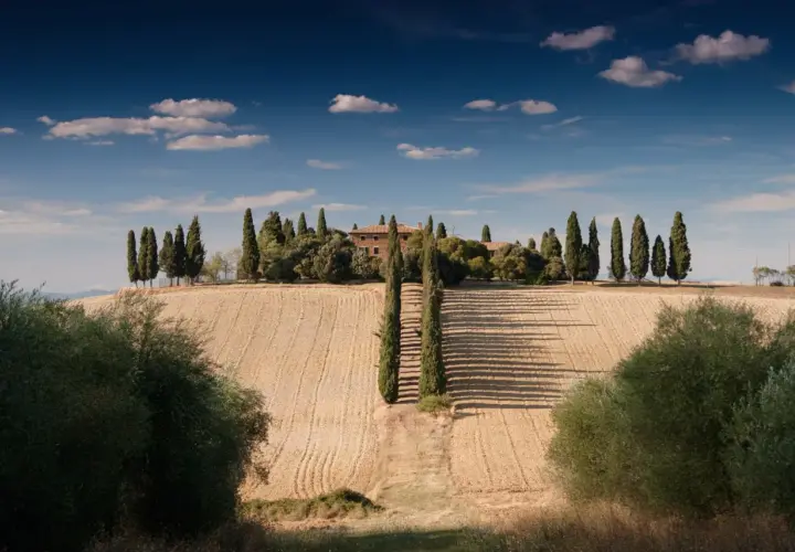 Dom toscano immerso nel verde, un sogno di agriturismo in Italia. Cipressi e campi dorati sotto un cielo azzurro.
