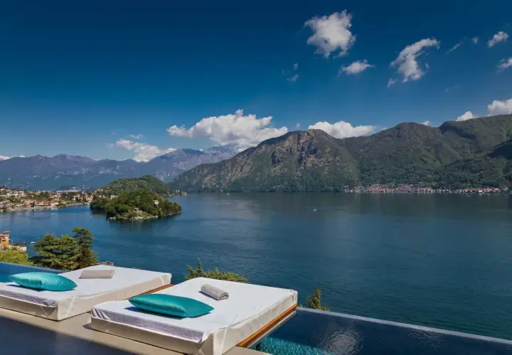 Vue panoramique sur un lac et des montagnes, avec des chaises longues et une piscine à débordement. Idéal pour des gîtes en Italie du Nord.
