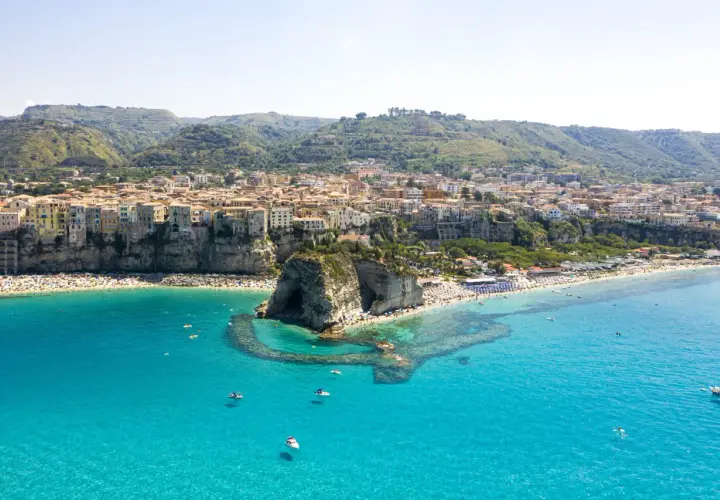 Vue aérienne de Tropea, avec ses maisons colorées perchées sur la falaise, une plage bondée et la mer d'un bleu turquoise éclatant.