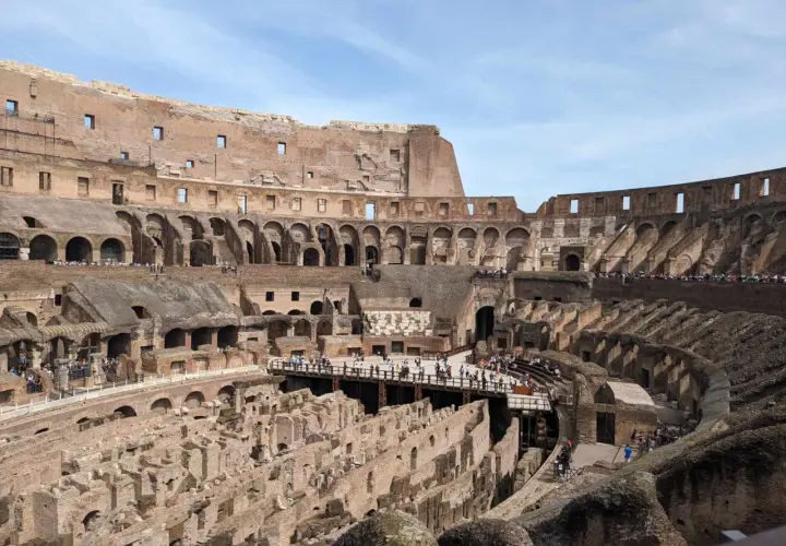 Vue intérieure du Colisée de Rome, vestiges de l'arène et des gradins, avec des touristes explorant ce monument historique.
