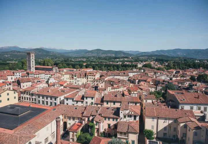 Vue aérienne de Lucques, avec ses toits de tuiles rouges et la tour de Guinigi se détachant sur les collines verdoyantes.