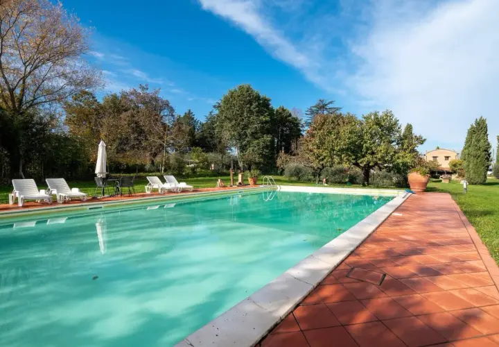 Piscine d'un gîte en Italie, entourée de verdure et de transats. Idéal pour des vacances paisibles.