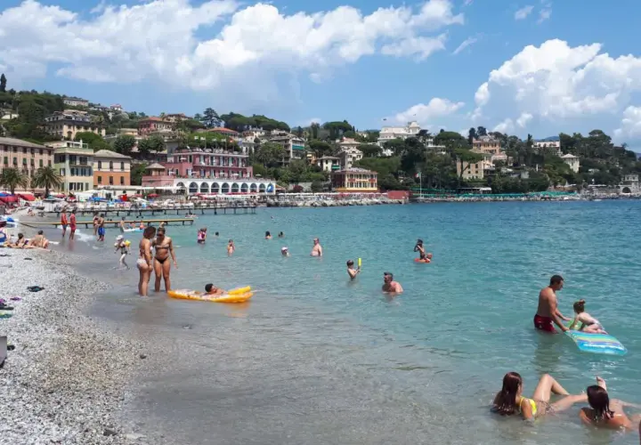 Journée ensoleillée à la plage Santa Margherita Ligure, baigneurs profitant de la mer turquoise et des bâtiments colorés en arrière-plan.