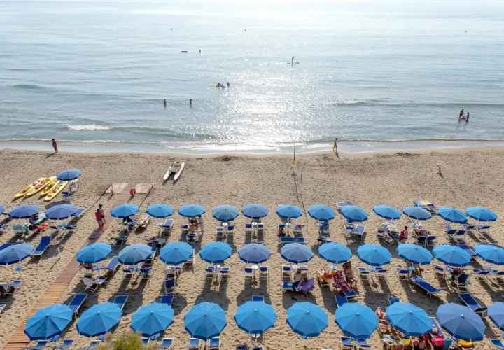Plage de San Vincenzo en Toscane, avec des rangées de parasols bleus, des kayaks et des gens profitant de la mer.
