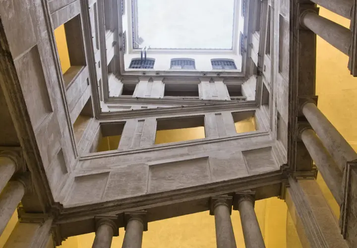 Vue en contre-plongée de l'escalier monumental du Palazzo Barberini, avec ses colonnes imposantes et ses fenêtres lumineuses.