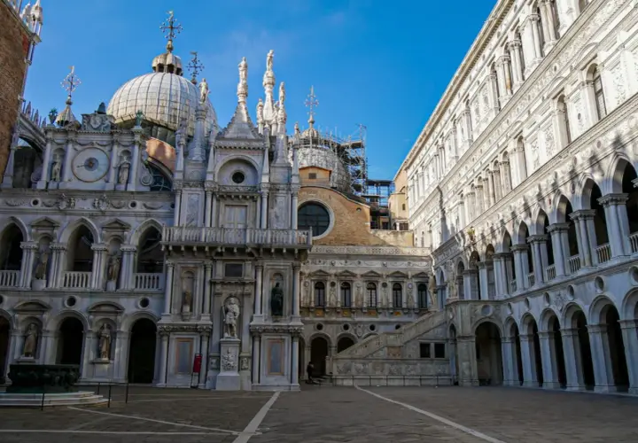 Le **Palais des Doges** à Venise, avec ses dômes, statues et arcades, se dresse majestueusement sous un ciel bleu.