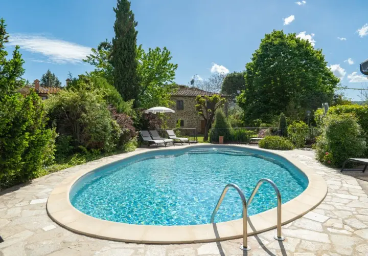 Magnifique piscine dans un jardin luxuriant, typique d'une location en Toscane. Le soleil brille sur l'eau bleue, invitant à la détente.