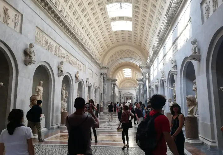 Visiteurs admirant des sculptures dans un long couloir orné de bustes et de bas-reliefs. Une excellente façon de savoir comment aller au Vatican.