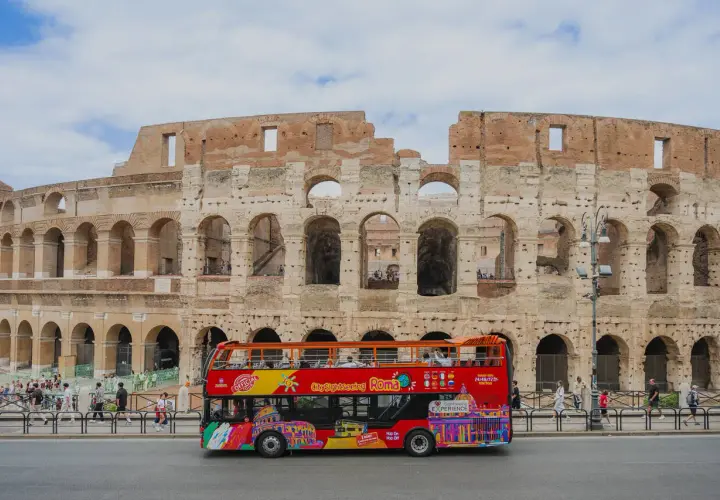 Un bus touristique rouge vif circule devant le Colisée à Rome, transportant des visiteurs pour une visite de la ville.