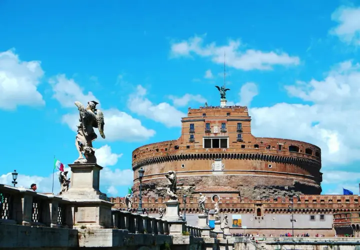 Le **château** Sant'Angelo à **Rome**, avec ses statues d'anges sur le pont, se dresse sous un ciel bleu éclatant.