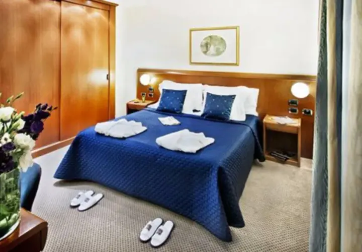 Chambre confortable à l'hôtel Ponte Sisto Rome avec lit bleu, peignoirs et pantoufles.