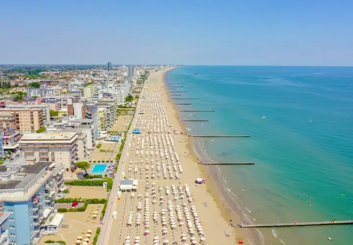 Vue aérienne de la longue plage de Lido di Jesolo, avec des rangées de parasols blancs, des hôtels et la mer Adriatique bleue.