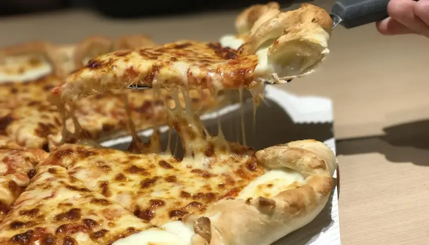 Une part de pizza romaine dégoulinante de fromage fondant est soulevée. Un délice à partager, comme à Rome.