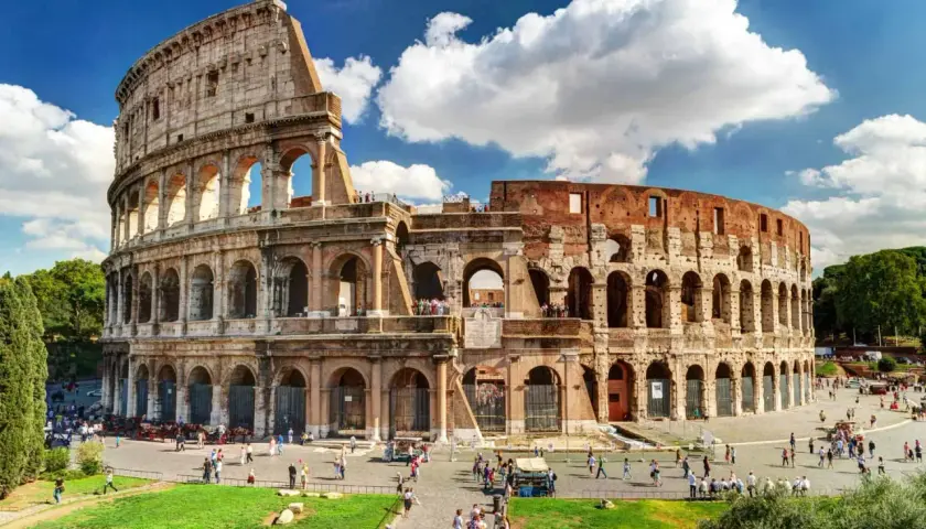Le Colisée de Rome en août, baigné de soleil, accueille des visiteurs sous un ciel bleu parsemé de nuages.