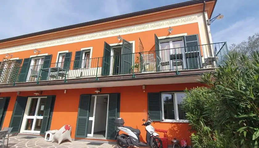 Façade orange vif de l'hôtel Olivium La Spezia avec balcons, volets verts et scooter blanc sur la terrasse pavée.