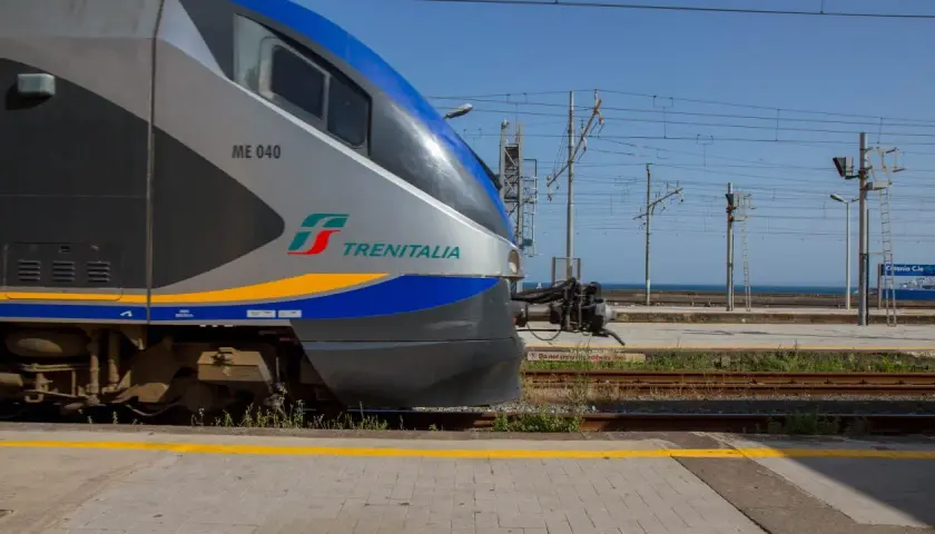 Le train Trenitalia ME 040, prêt à partir pour un voyage en train en Sicile, attend sur les rails sous un ciel bleu clair.