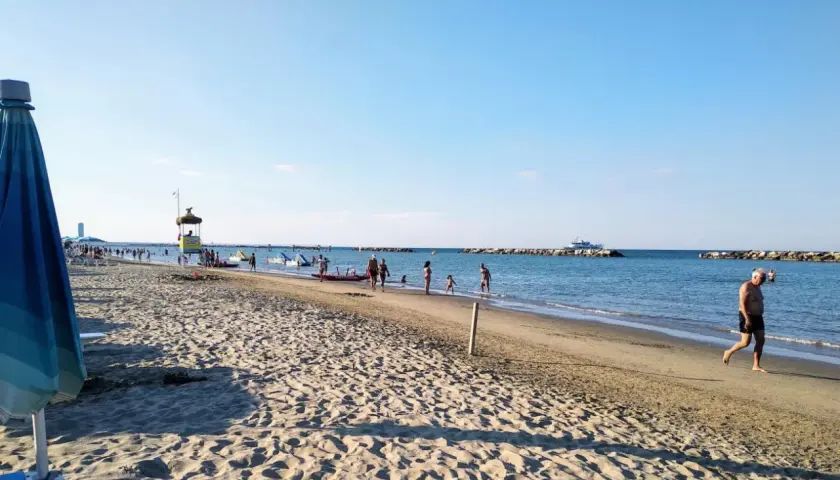 Plage animée à Gatteo Mare, avec des baigneurs, des enfants jouant dans l'eau et un poste de secours. Un bateau navigue au loin.
