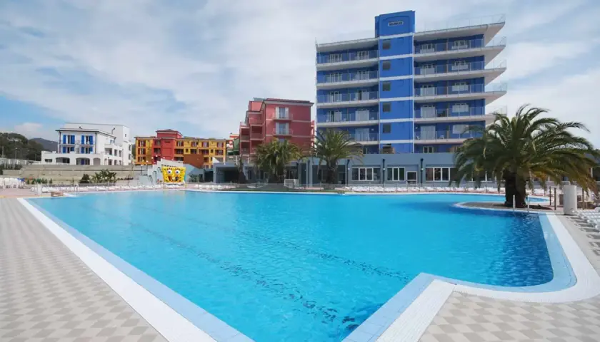 Vaste piscine bleue devant des bâtiments colorés et un grand gonflable de Bob l'éponge, au village ai pozzi.