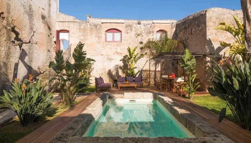 Cour intérieure d'une masseria en Italie, avec piscine, mobilier de jardin et végétation luxuriante.