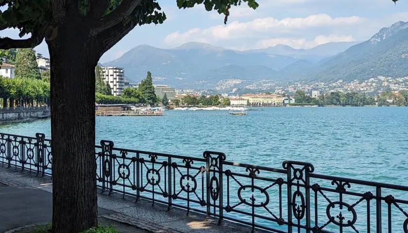 Vue paisible du lac de Lugano, avec une promenade bordée d'arbres et de montagnes en arrière-plan.