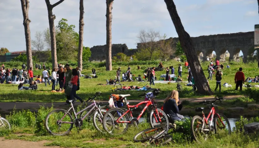 Des vélos garés près d'un parc à Rome, où des gens profitent du soleil et des ruines antiques.