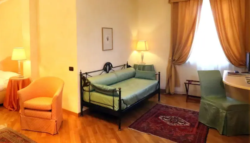 Chambre confortable dans un des hôtels de Castiglione Tinella, avec un lit de repos vert, un fauteuil orange et des rideaux dorés.