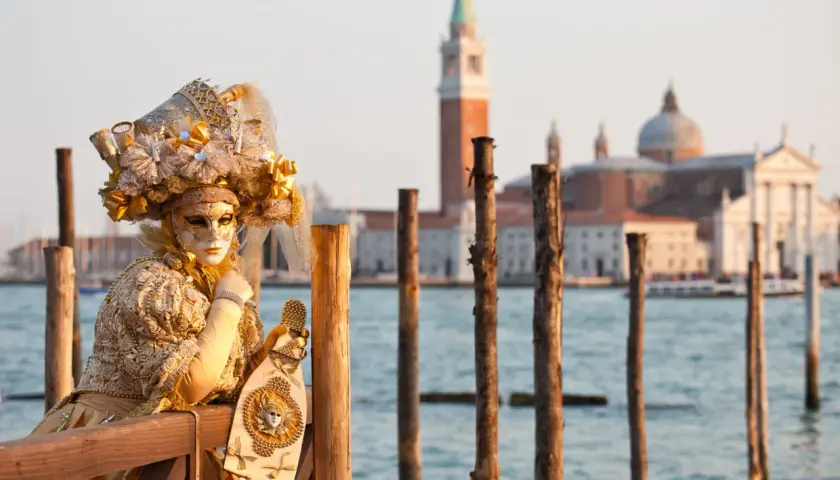 Une personne masquée et costumée, prête pour le carnaval, pose près de l'eau. Une belle image pour savoir quand aller à Venise.