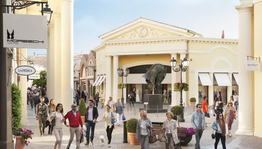 Des promeneurs profitent d'une journée ensoleillée au Castel Romano Outlet, admirant les vitrines et l'art.