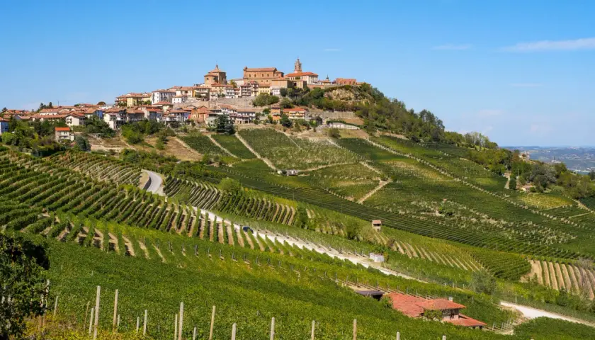 Vue panoramique de La Morra, Italie, avec ses vignobles en terrasses ondulant sur les collines, menant à un village pittoresque couronnant la crête.