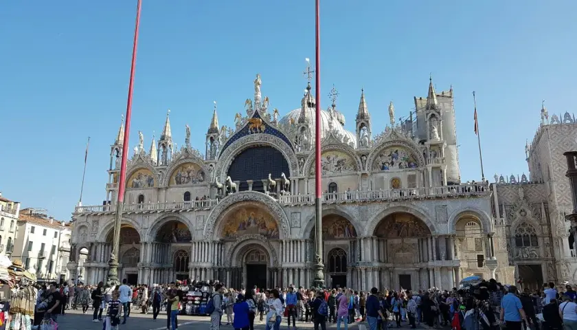 La place animée devant la magnifique église de Venise, avec ses dômes et ses mosaïques, sous un ciel bleu éclatant.