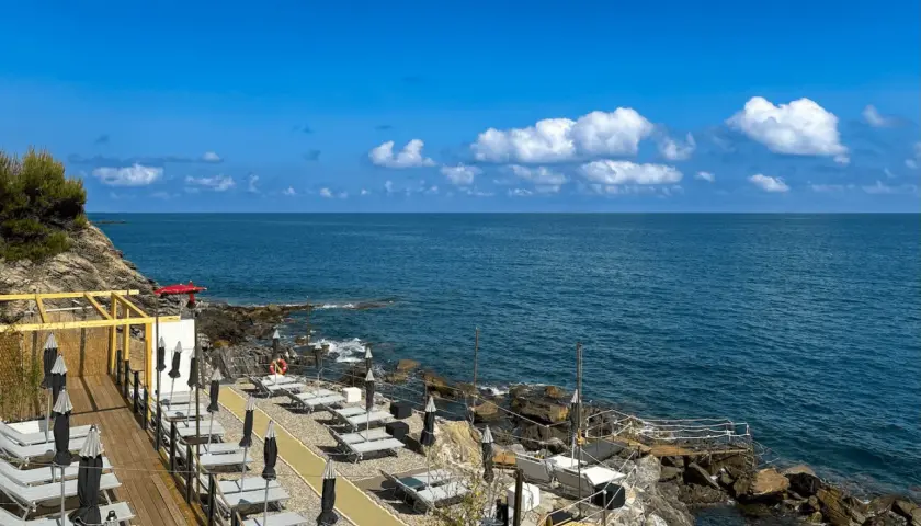 Plage aménagée à San Bartolomeo al Mare, avec chaises longues et parasols face à la mer bleue sous un ciel d'été.