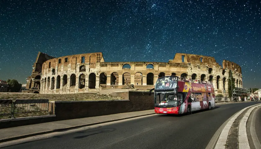 Un bus de nuit Rome passe devant le Colisée sous un ciel étoilé.