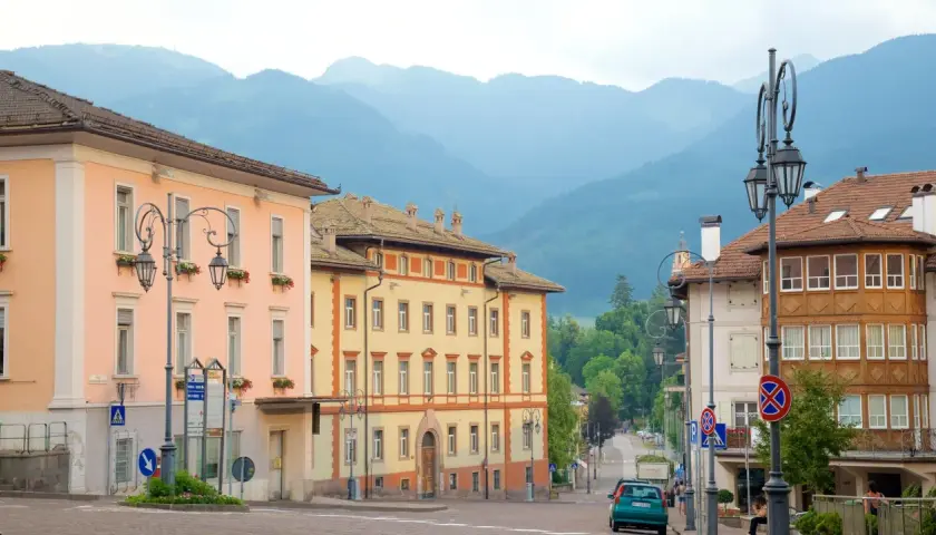 Vue d'une rue à Cavalese, Italie, avec des bâtiments colorés et des montagnes en arrière-plan.