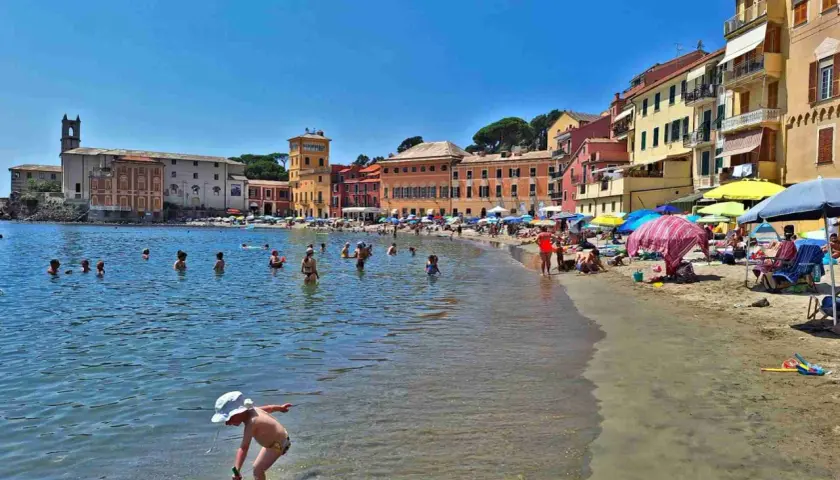 Plage animée à Chiavari, Italie, avec des baigneurs dans l'eau et des parasols colorés sur le sable.