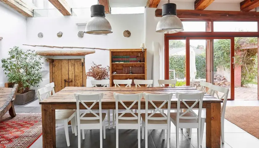 Salle à manger rustique d'un agriturismo en Ligurie, avec table en bois massif, chaises blanches et grande porte vitrée donnant sur le jardin.