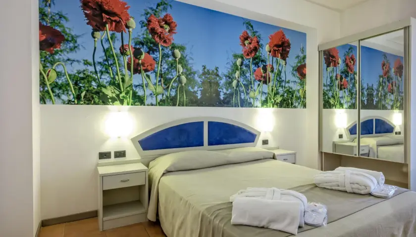 Chambre d'hôtel Antares Sicile avec fresque de coquelicots rouges. Peignoirs blancs et chaussons prêts pour les clients.