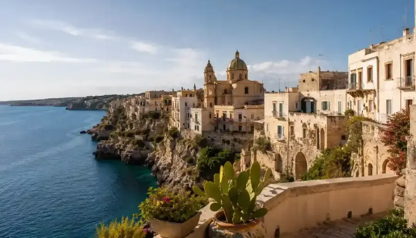 Vue d'une ville côtière italienne perchée sur une falaise, avec des maisons blanches et une église. Idéal pour une maison à louer en Italie.