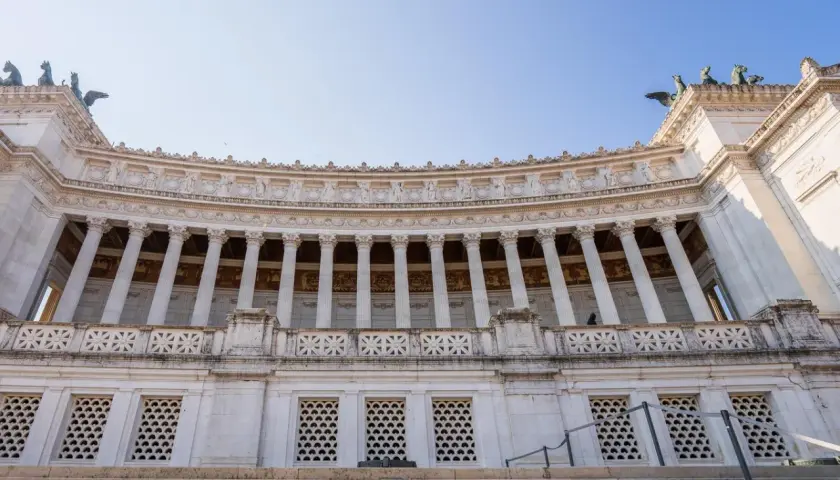 Majestueux monument à Victor-Emmanuel II à Rome, avec ses colonnes imposantes et ses sculptures, sous un ciel bleu clair.