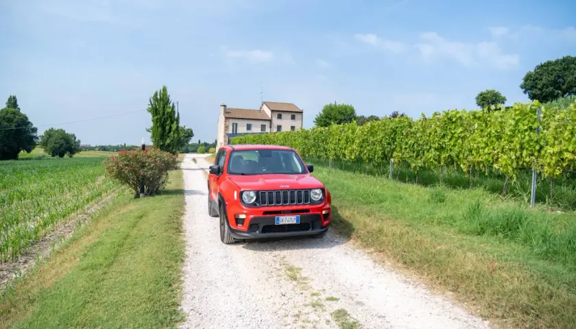Une voiture rouge Jeep sur un chemin de gravier en Italie, près d'un vignoble. Le prix de cette voiture est très attractif.