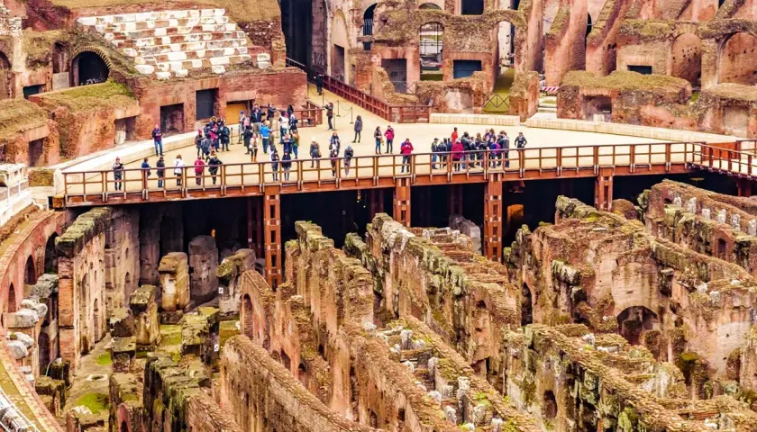 Vue d'ensemble de l'arène du Colisée à Rome, avec des touristes sur une passerelle surplombant les ruines antiques.